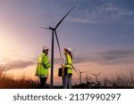 Engineer wearing uniform ,helmet inspection and survey work in wind turbine farms rotation to generate electricity energy. Green ecological power energy generation wind sustainable energy concept.