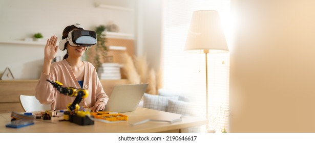 Engineer wearing (VR)virtual reality headset and gesturing while sitting at home.engineer is working on innovative technology mechanical Robot arm,She using laptop controlling Robotic arm by her hand.