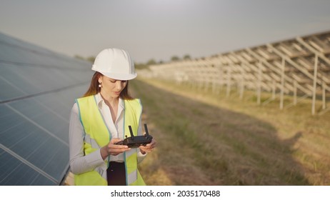 Engineer Woman In Hardhat Holding Tablet Computer Operating Flying Drone In Solar Plant. Photovoltaic Solar Panel Installation. Solar Array. New Technologies. The Investor Checks The Solar Power