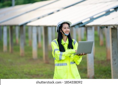 Engineer Women Wearing Safety Vest And Safety Helmet Holding Laptop Computer Working In Front Of Solar Panels,Photovoltaic Cell Park,Green Energy Concept.