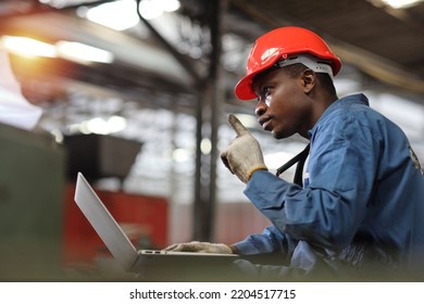 Engineer Or Worker Man In Protective Uniform Sitting And Using Computer While Pose Thinking Something And Controlling Work With Hardhat And Electric Cable Line At Heavy Industry Manufacturing Factory