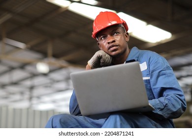 Engineer Or Worker Man In Protective Uniform Sitting And Using Computer While Pose Thinking Something And Controlling Work With Hardhat And Electric Cable Line At Heavy Industry Manufacturing Factory