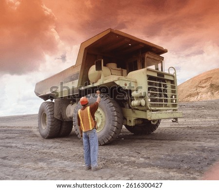 Engineer worker stand behind mining big monster truck.