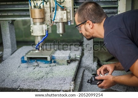 Engineer worker technician operating with CNC milling metal engraving machine in factory workshop.