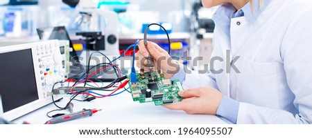 Engineer working with circuits. A woman engineer solders circuits sitting at a table. 
Microchip production factory. 
Girl repairing electronic device on the circuit board.