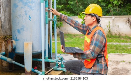 Engineer Working In Drinking Water Factory Using A Laptop Computer To Check Water Management System And Boiler Water Pipe  Outside The Factory