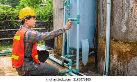 Engineer Working In Drinking Water Factory Using A Laptop Computer To Check Water Management System And Boiler Water Pipe  Outside The Factory