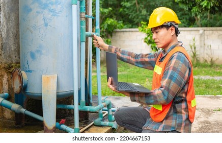 Engineer Working In Drinking Water Factory Using A Laptop Computer To Check Water Management System And Boiler Water Pipe  Outside The Factory