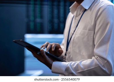 Engineer working in high tech server farm, using laptop and tablet to analyze data, ensuring seamless data flow. Man examining hardware in data center, ensuring system integrity and security, close up