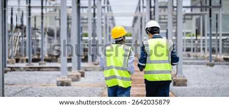 An engineer is working at high voltage power substation wearing safety gear while conducting inspection and check of electrical infrastructure to ensure proper operation and safety
