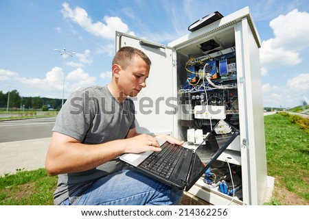engineer working with laptop outdoors adjusting communication equipment in distribution box