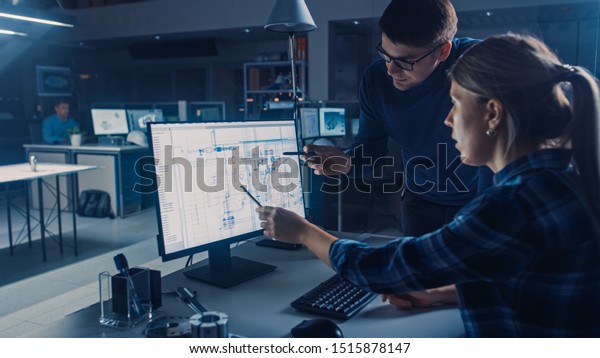 Engineer Working on Desktop Computer, Screen\
Showing CAD Software with Technical Blueprints, Her Male Project\
Manager Explains Job Specifics. Industrial Design Engineering\
Facility Office