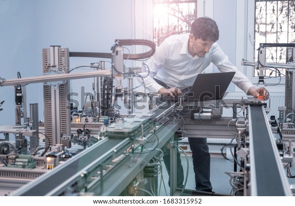 Engineer is working on laptop to program smart\
factory prototype\'s automation. Automated car on production line,\
artificial intelligence in smart manufacturing. Industry 4.0\
concept.