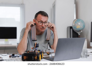 Engineer working on a robotics project, experiencing technical difficulties and looking confused at the laptop screen