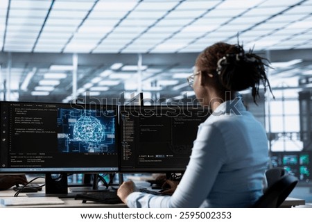 Engineer working at PC desk, doing checkup on AI server room providing computing resources. African american IT professional investigating data center mainframes using computer