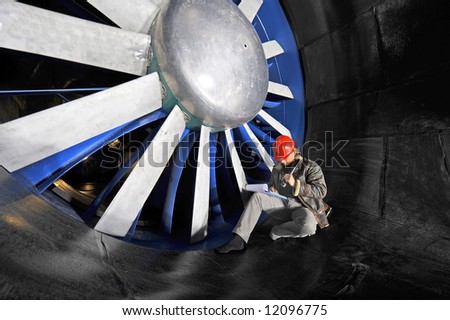 An engineer working through a checklist on a clipboard in front of the huge blades of a wind tunnel