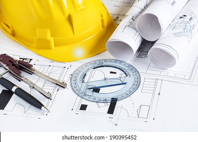 Engineer workplace with blueprints, compass, pen, protractor  and safety helmet