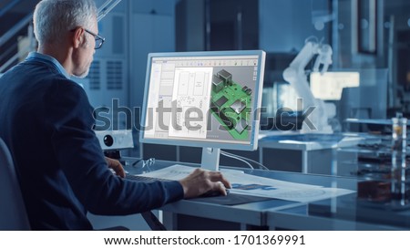 Engineer Works on Computer Uses CAD Software to Design 3D Industrial Machinery Component. In the Background Robot Arm Concept Standing in Heavy Industry Engineering Facility. Over the Shoulder Shot