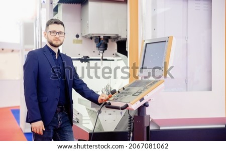 Engineer young man in glasses operates CNC automatic metalworking lathe or laser, industrial worker in modern factory.