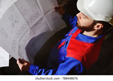 Engineer-builder working with documents on the construction site. Worker inspects drawings on the construction site against the background of factory equipment