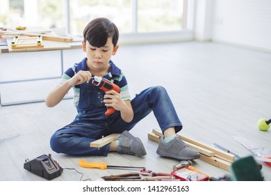 Engineering concept - A boy is using a drill driver to drill the wooden with the carpenter's equipment placed around.