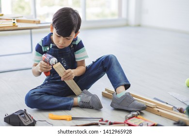 Engineering concept - A boy is using a drill driver to drill the wooden with the carpenter's equipment placed around.