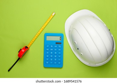 Engineering Construction Safety Helmet And Calculator, Ruler On Green Background. Calculation Of The Cost Of Repair Or Building A House. Top View. Flat Lay