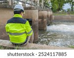 A engineering doing his checking routine. He is wearing hard hat and engineer uniform.Standing by the rail by the dam.Monitor water levels from the heavy rain that has been falling for several days.