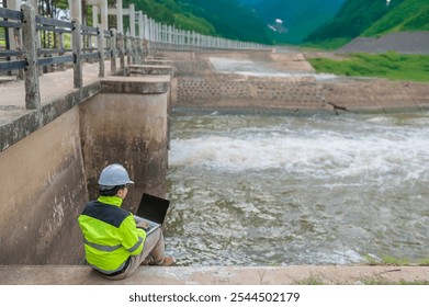 A engineering doing his checking routine. He is wearing hard hat and engineer uniform.Standing by the rail by the dam.Monitor water levels from the heavy rain that has been falling for several days.