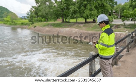 A engineering doing his checking routine. He is wearing hard hat and engineer uniform.Standing by the rail by the dam.Monitor water levels from the heavy rain that has been falling for several days.
