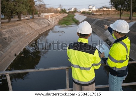 A engineering doing his checking routine. He is wearing hard hat and engineer uniform.Standing by the rail by the dam.Monitor water levels from the heavy rain that has been falling for several days.