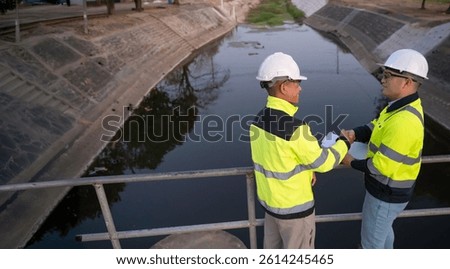 A engineering doing his checking routine. He is wearing hard hat and engineer uniform.Standing by the rail by the dam.Monitor water levels from the heavy rain that has been falling for several days.