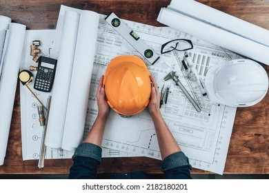 Engineering holding safety helmet  with drawings inspection on the office desk and Calculator, triangle ruler, safety glasses, compass, vernier caliper on Blueprint. Engineer, Industry concept. - Shutterstock ID 2182180201