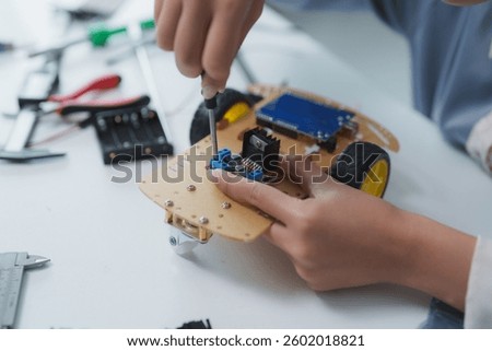 Engineering student assembling programmable robotics toy car using screwdriver and other components on white table in innovation laboratory