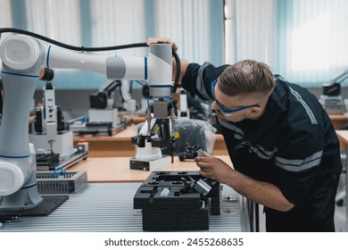Engineering student assembling a robotic arm using a computer in a technology workshop. Service engineer holding a robot controller and inspecting the robotic arm's welding hardware.