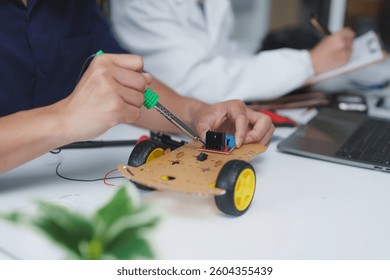 Engineering students are assembling a robot car prototype using a soldering iron and electronic components in a modern laboratory, showcasing innovation and collaboration in robotics education