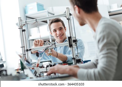 Engineering Students Working In The Lab, A Student Is Adjusting A 3D Printer's Components, The Other One On Foreground Is Using A Laptop