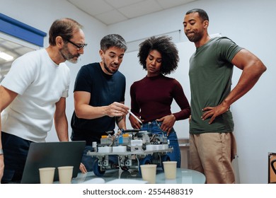 Engineering team examining a robot prototype, discussing its electric circuit and making improvements in a collaborative work environment