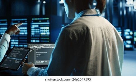 Engineering team members running code on tablet and laptop, updating professional data center equipment designed to accommodate server rigs, networking systems and storage arrays