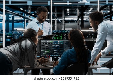 Engineering team programming in AI data center housing advanced equipment used for machine learning training. Server farm workers running code on PC to upgrade artificial intelligence systems