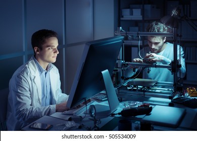 Engineering Team Working In The Lab At Night, A Student Is Working With A Computer And The Other One Is Adjusting A 3D Printer's Components