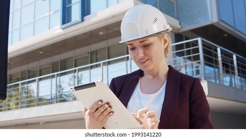 Engineering woman working in outdoor city background. Portrait of beautiful female architectural engineer in hardhat using digital tablet on commercial building construction site