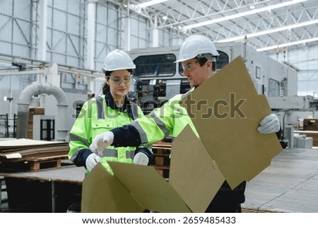 Engineers analyzing cardboard packaging inside spacious manufacturing facility. The image captures collaboration and technical precision in modern industrial environment.