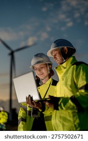 Engineers analyzing smart grid data via laptop at onshore wind farm. Integrating AI technology to drive the global clean energy transition.