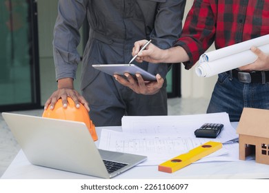 Engineers and architects pointing at digital tablet screens. Two Construction Engineers or Architects discussing at work with digital tablet, laptop and blueprint on construction site.