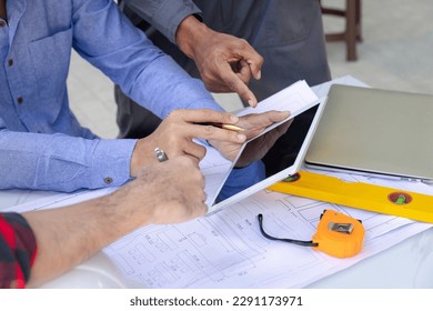 Engineers and architects pointing at digital tablet screens. Two Construction Engineers or Architects discussing at work with digital tablet, laptop and blueprint on construction site.