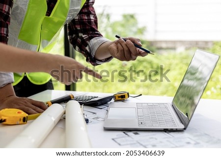 Engineers and architects pointing at laptop screens looking at blueprints to make some modifications, they meet together to plan construction and fixes. Design and interior design ideas.