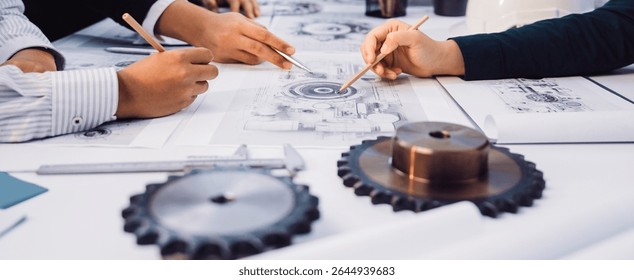 Engineers collaborate on mechanical designs, using tools and blueprints in a professional workspace. Their hands create sketches while gears and equipment surround them. SACTR
