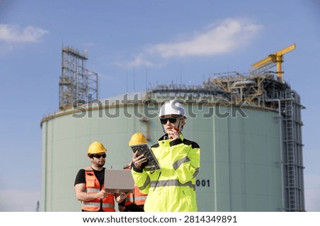 Engineers collaborating at construction site with safety gear monitoring progress of industrial project against clear sky