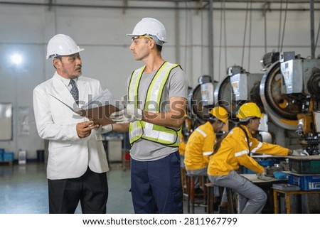 Engineers collaborating on a project in an industrial setting with employees engaged in various tasks in the background